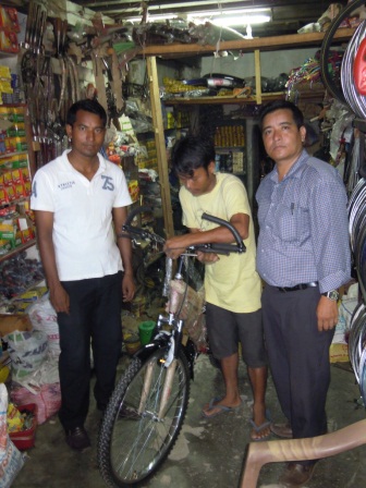 Na een jaar trouwe dienst krijgt Ruben Pariyar (wit shirt) een fiets, wat hem in staat stelt nog meer goed werk te doen. De man met de blauwe bloes is Dhruba Adhikari, onze secretaries in Nepal